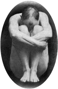 Aleister Crowley sentado no chão, abraçando as pernas, com a cabeça abaixada entre os joelhos.